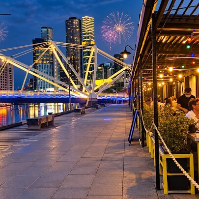 A view down the footpath at South Wharf, Melbourne, showing the outdoor tables of BangPop on the right and a lit up bridge with fireworks in the night sky.