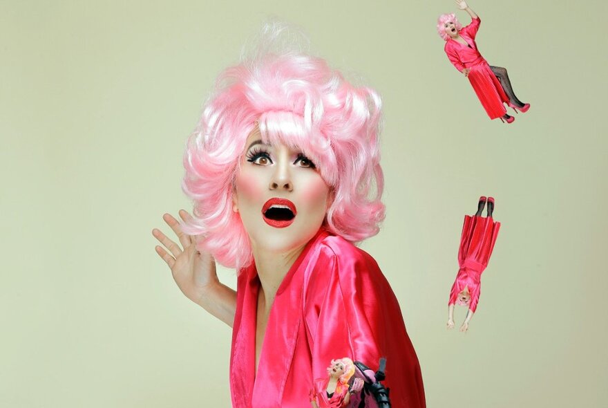 Comedian wearing pink blonde wig, looking aghast at falling tiny figures of herself.