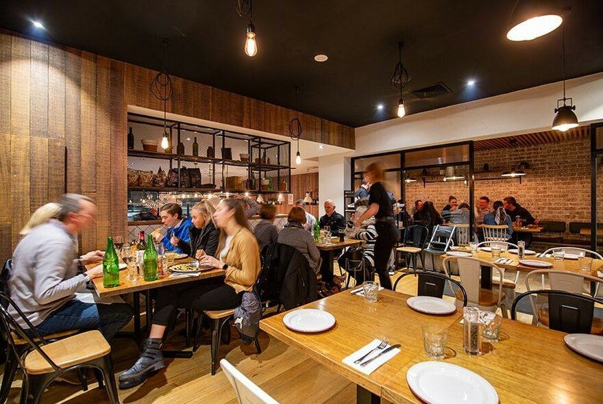 Restaurant interior with wooden walls and shelving, diners eating at tables.