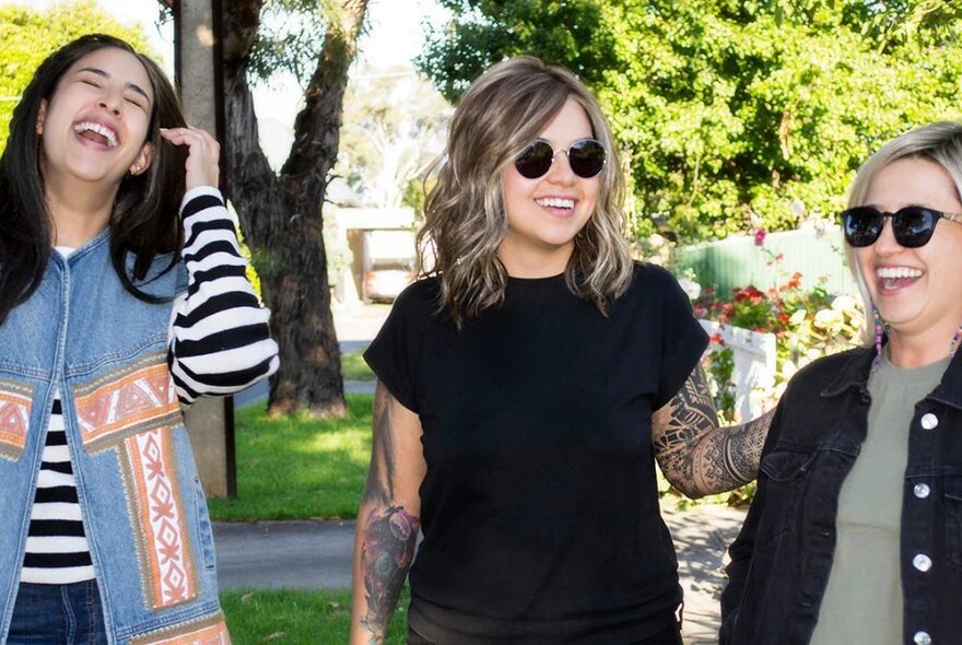 Three women outside laughing together in the sun. 