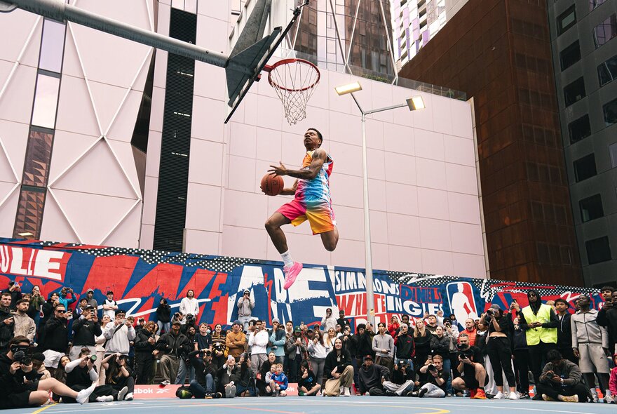 A basketballer leaping into the air for a slam dunk while crowds watch.