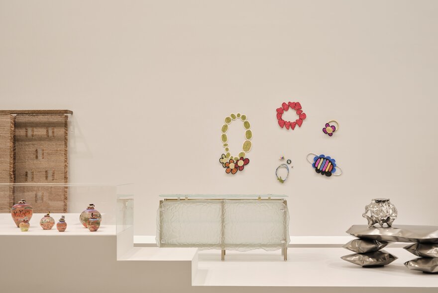 Creative design artworks displayed in a white gallery setting, with some artworks hanging on the wall and others on a white dais.