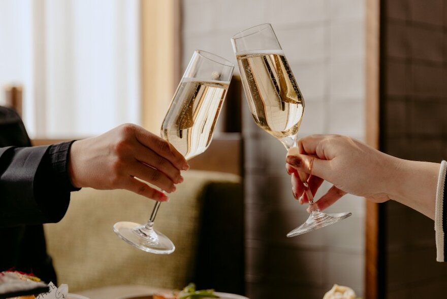 Two people making a toast with clear, angular crystal champagne flutes filled with sparkling wine.