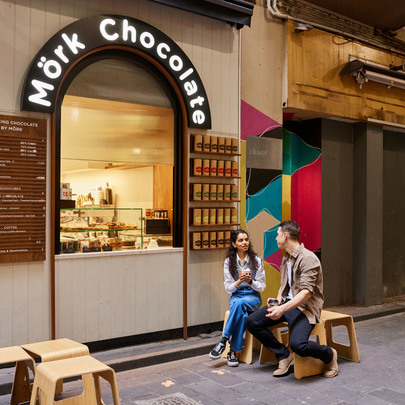A man and woman sitting on stools outside a hole-in-the-wall cafe in a laneway.