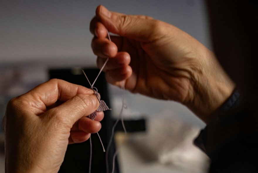 A pair of hands threading a needle with cotton.