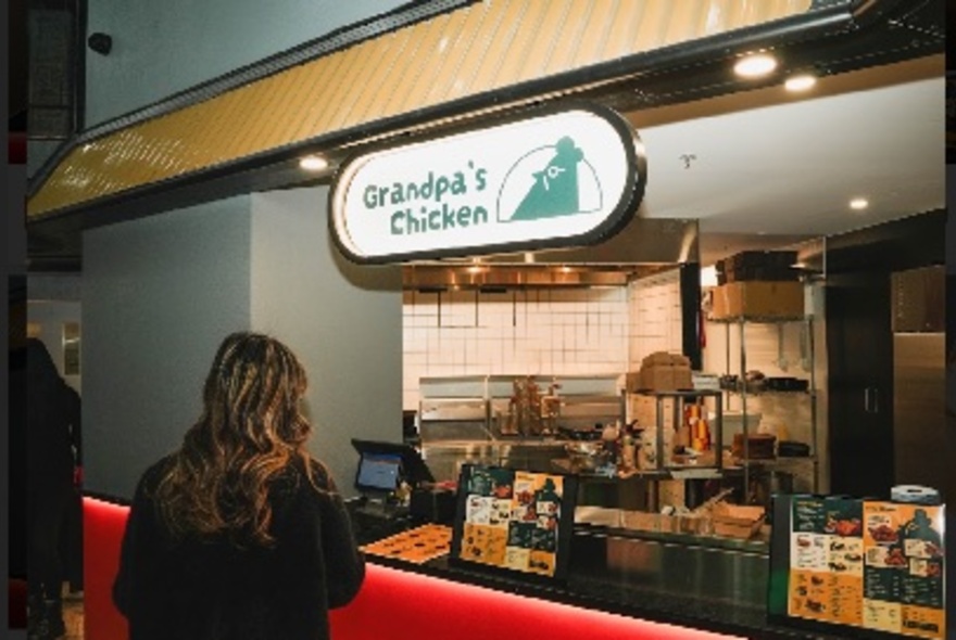 People waiting at the counter to order food, looking into an open kitchen.