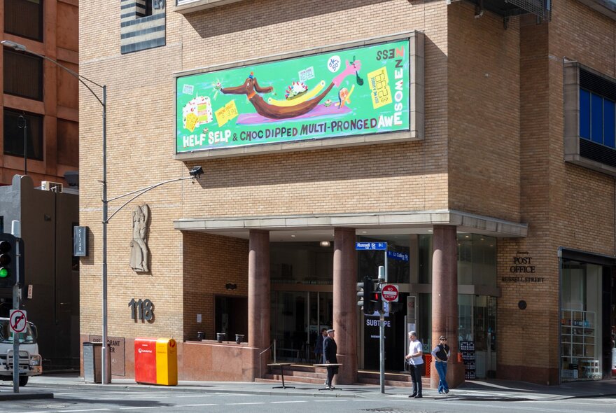 Brightly coloured artwork on the cream brick facade of the Hero apartment building, with passers-by on the road below, a street lamp and two letterboxes.