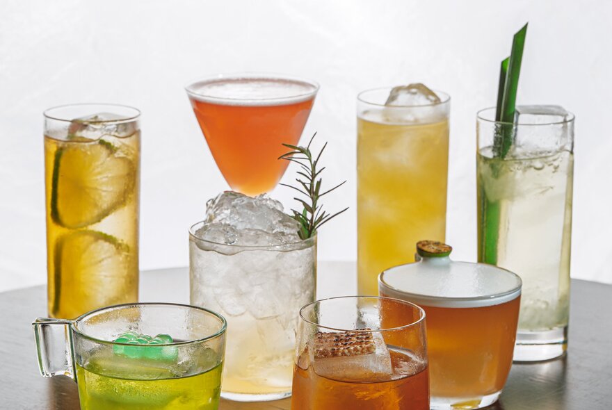 A selection of cocktails in different shaped glasses, resting on a table, against a pale background.