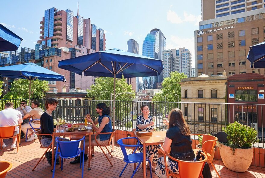 People sharing drinks at orange and blue tables on a sunny rooftop.