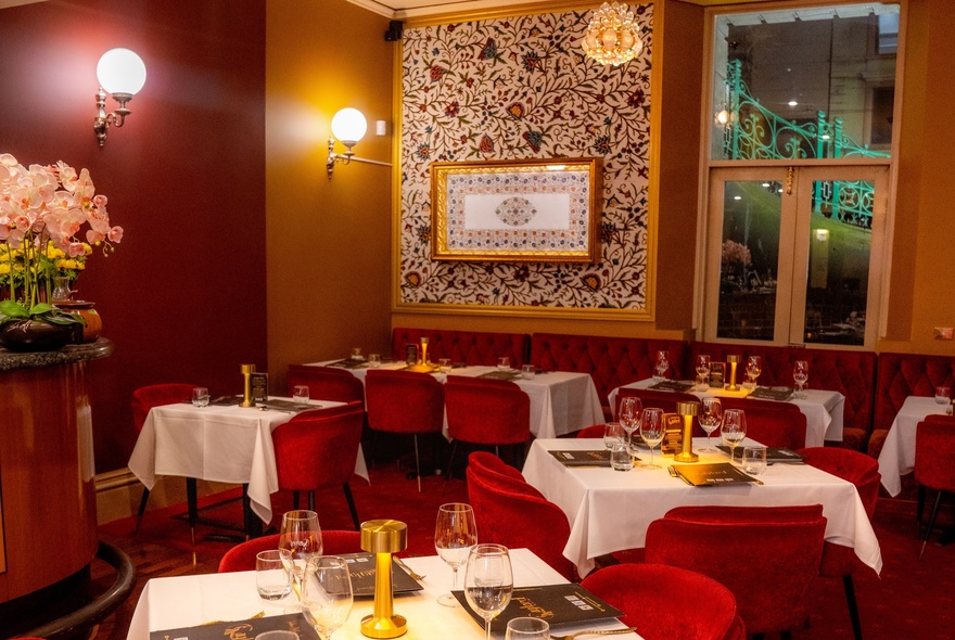 Intimate restaurant interior with lamp lighting and white-clothed tables with red chairs.