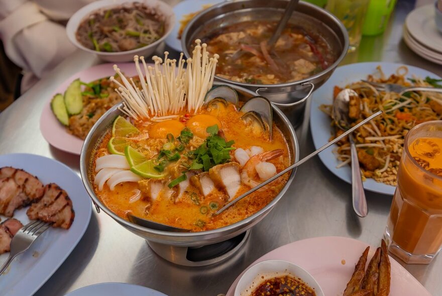 A big bowl of Thai hot pot with seafood, pork, noodles and mushrooms in it.