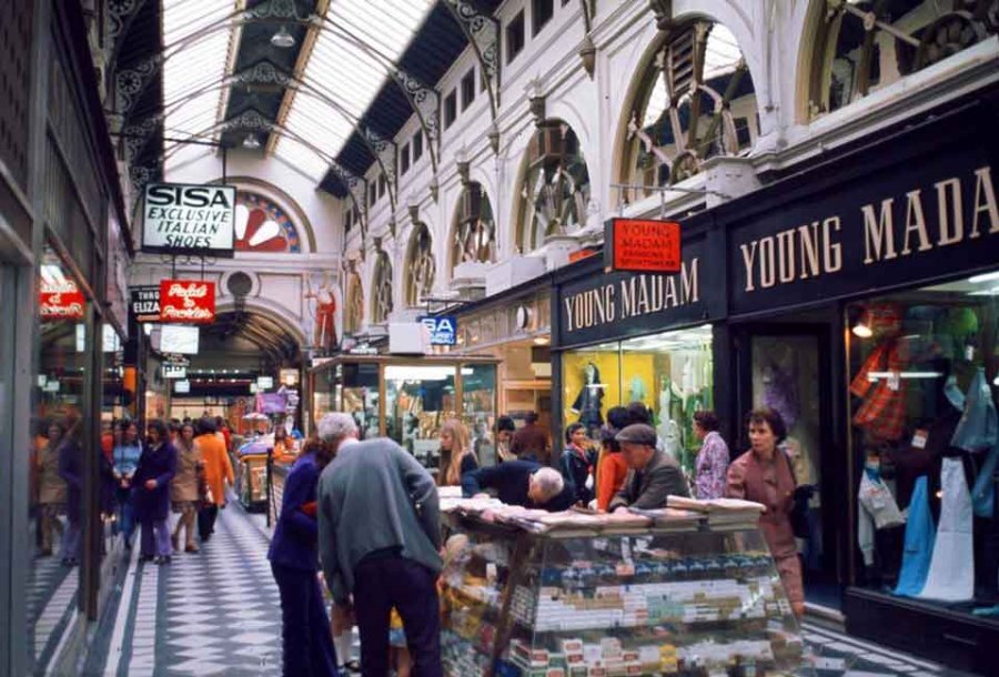 An old photo of people shopping in an arcade.