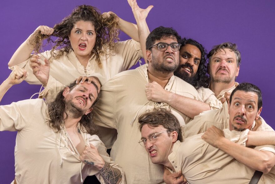 A group of actors dressed in beige clowning around for a group photo. 