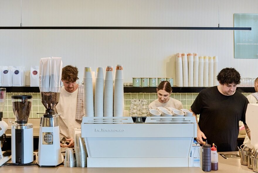 Cafe staff preparing food behind a counter and pale blue coffee machine with cups and bean roasters.