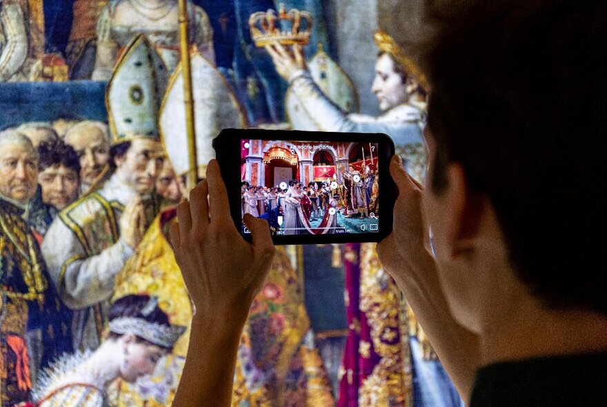 A museum patron using a HistoPad, an augmented reality device, to learn more about a historical artwork seen behind the screen.