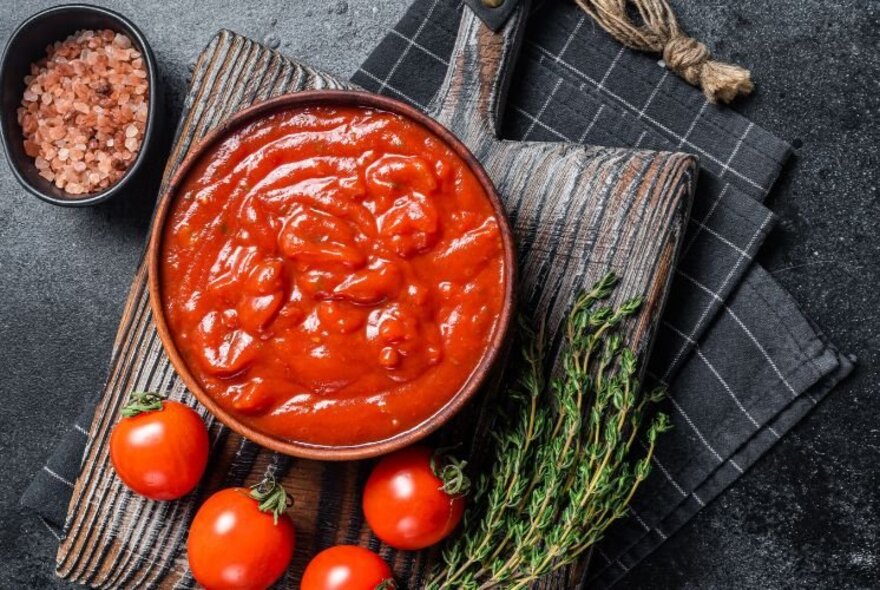 Looking down on a bowl of sugo and four tomatoes scattered around the bowl. 