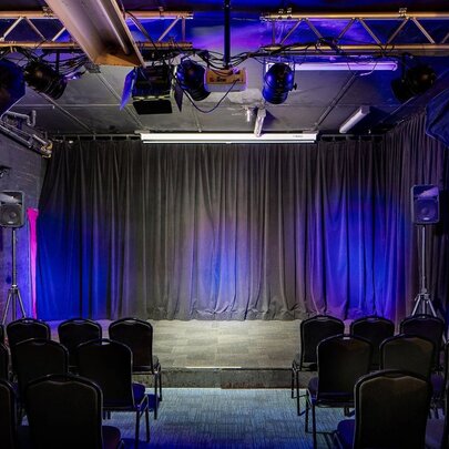 An empty stage with a black curtain, seen from behind the rows of empty chairs.