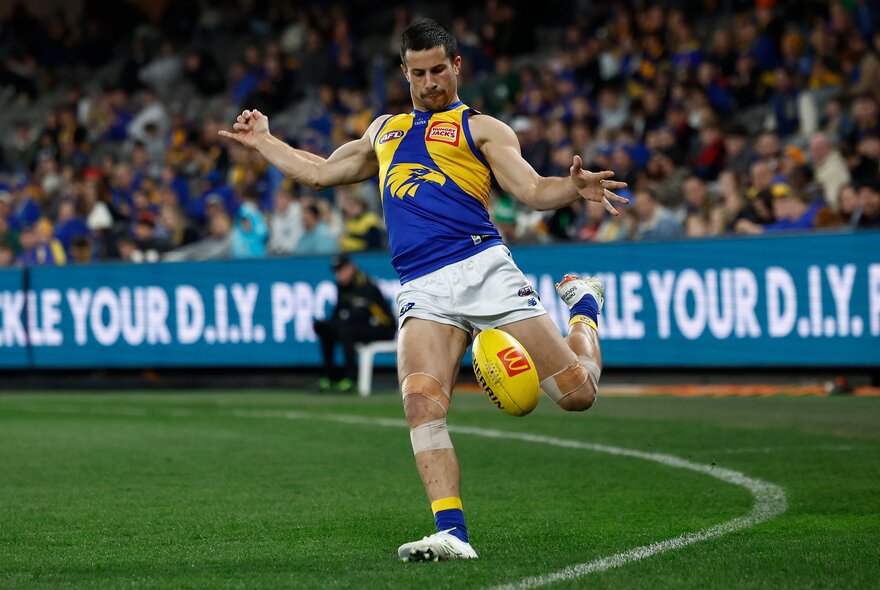 West Coast Eagles AFL football player running and kicking a football during a match.