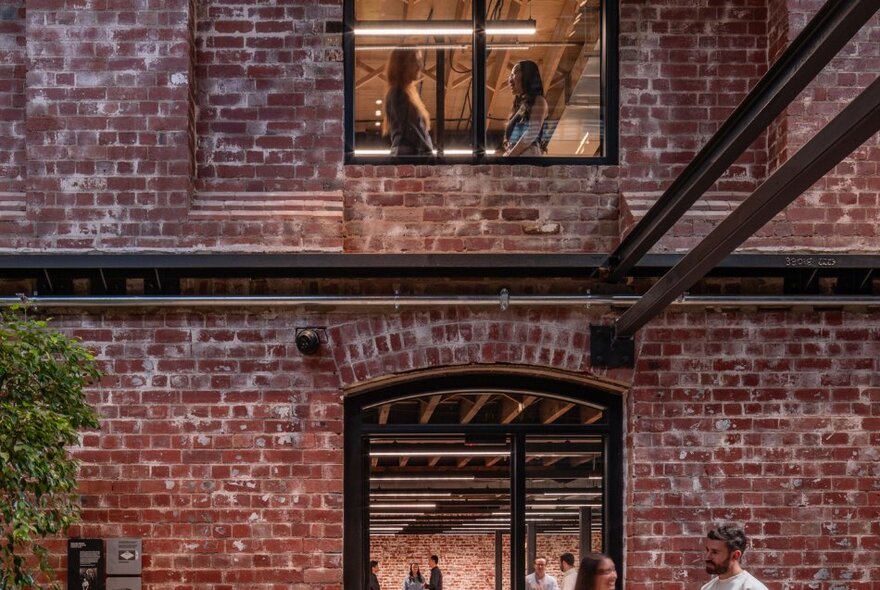 People inside and outside red brick industrial building with metal supports.