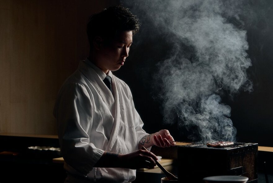 Chef using a utensil to cook food at a portable grill with steam rising into the air.