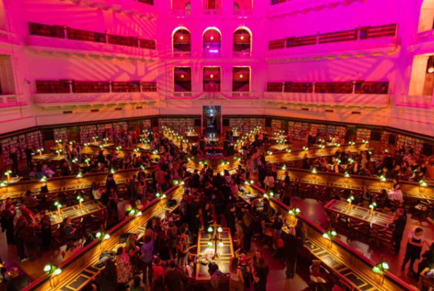 State Library Victoria Reading Room lit by pink lights and reading lamps on desks.