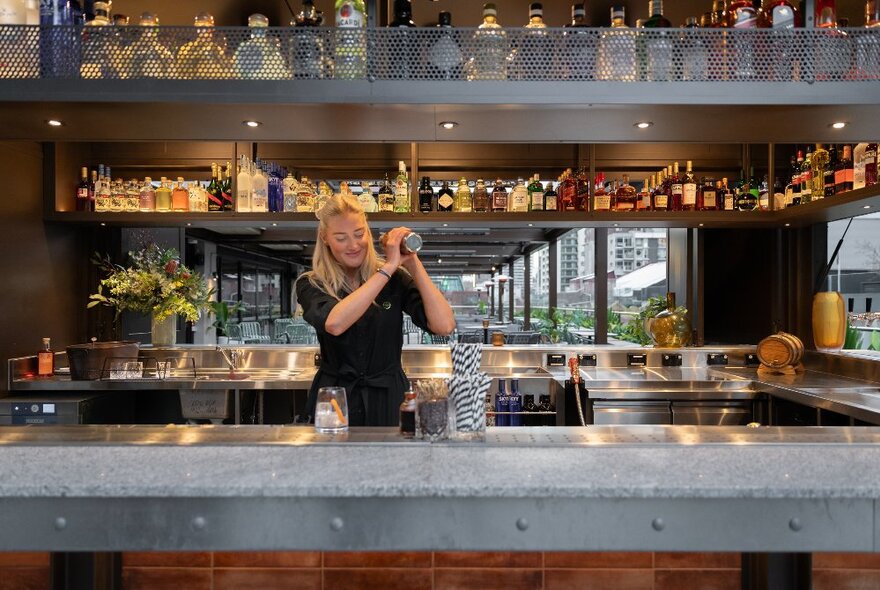 A bartender shaking a cocktail in a mixer using both hands,standing behind a well-stocked bar.