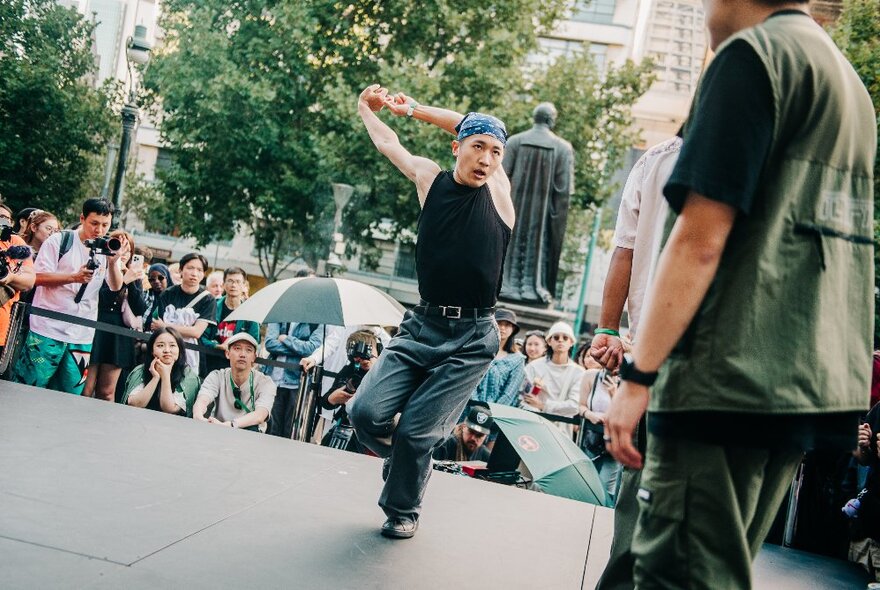 A hip-hop dancer performs outdoors in front of a small crowd. 