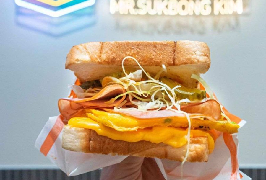 An egg sandwich with neon sign behind it 