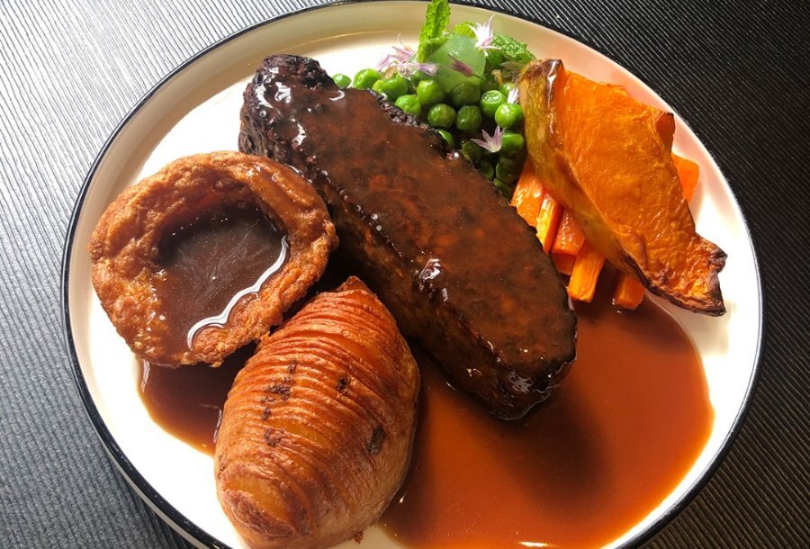 A nut roast dish with gravy, hasselback potato, vegetables and a Yorkshire pudding.