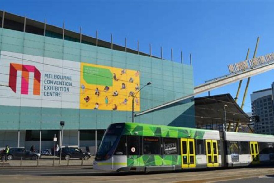 A tram passing the Melbourne Convention Centre exterior with signage and blue sky.