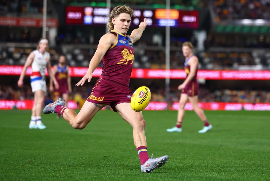 Brisbane Lions AFL football player kicking a yellow ball during a match.