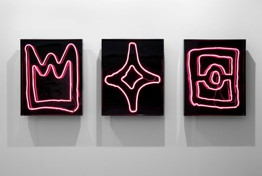 A series of three different artworks on a wall, each neon on a black background,