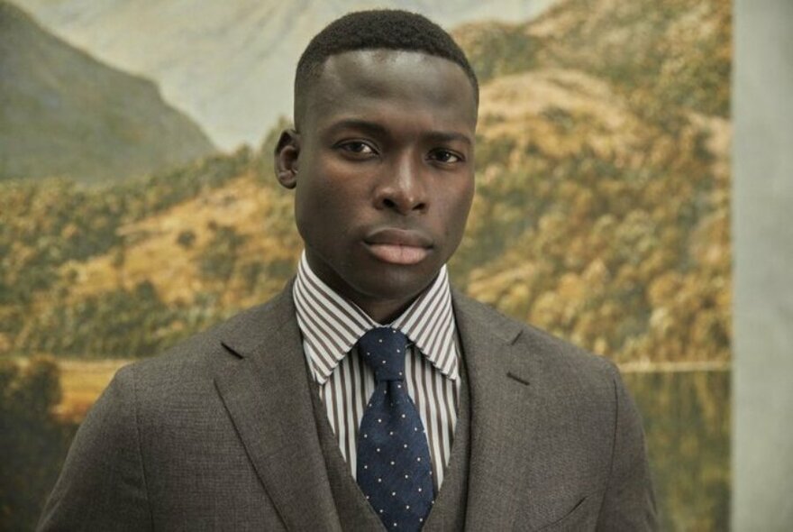 A model in a grey suit, vest, blue tie and striped shirt.