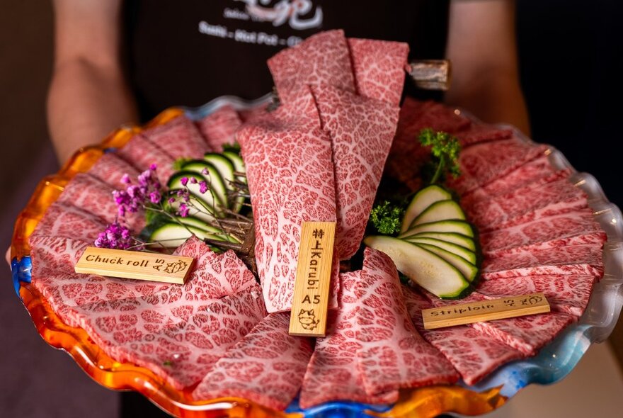 Waiter holding a platter of sliced wagyu meat arranged in circles with garnishes.