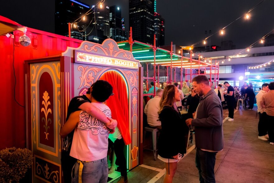 Couples in an outdoor arcade space at night with brightly lit stalls.