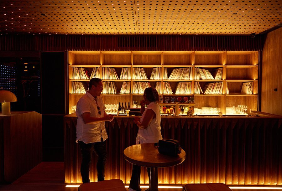 A couple in a dark bar with glowing shelves of records. 