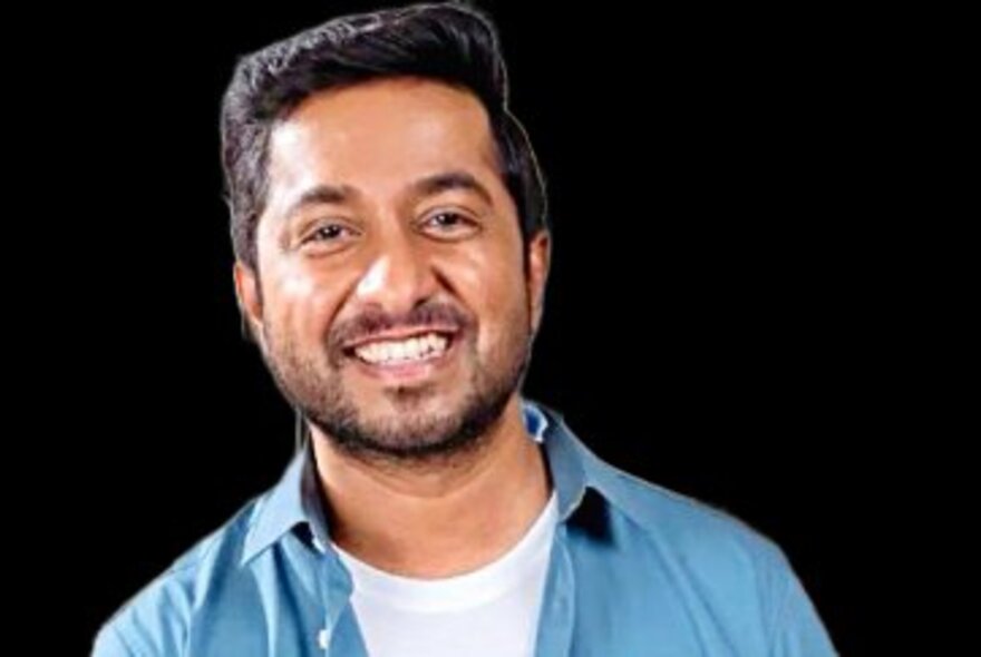 Actor and musician Vineeth Sreenivasan, a man aged about 40 years, wearing an open necked blue shirt, against a dark background, smiling at the viewer.