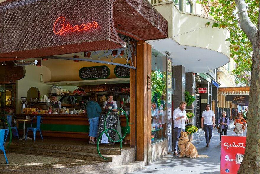 Outside a small grocer there is a man eating ice cream with his golden retriever dog