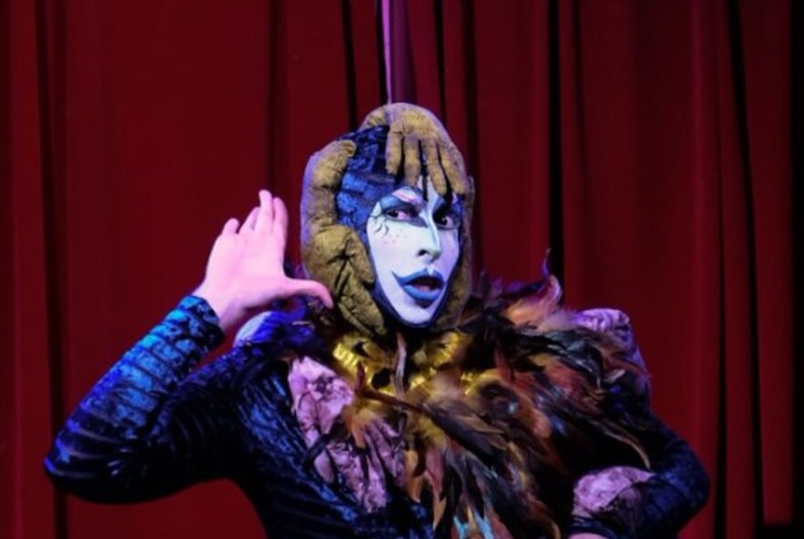 Drag performer wearing white and purple makeup and catsuit.