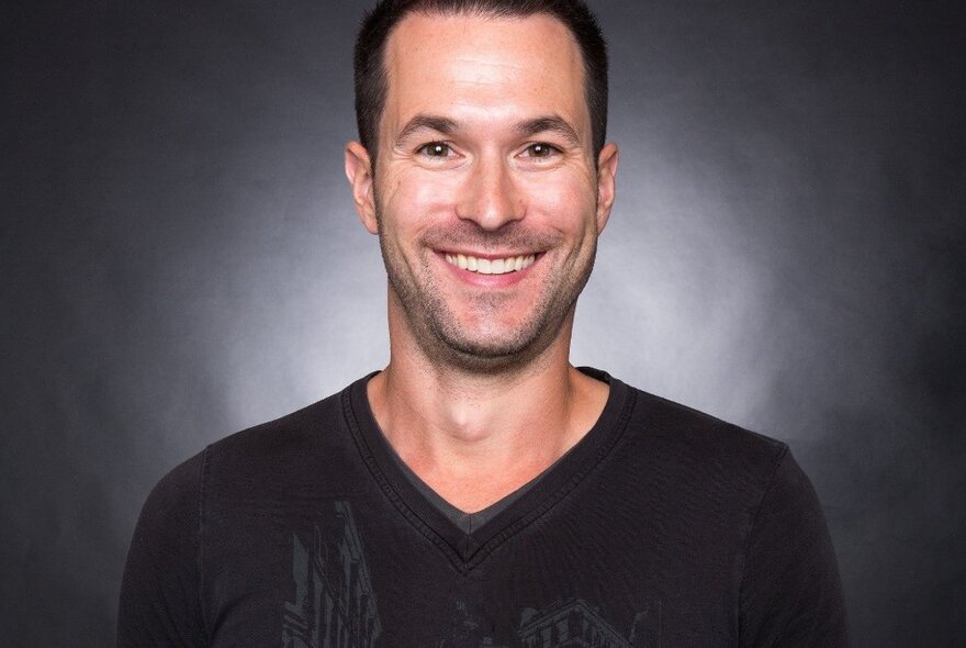 Game developer Ryan Warden smiling openly in front of a dark background with light emanating from behind. 