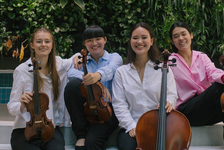 The four members of the Tarilindy Quartet smiling and posing with their instruments. 
