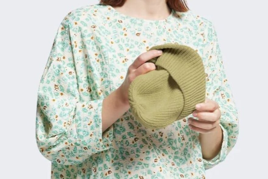 A model in a blue dress holding a light green knitted beanie.