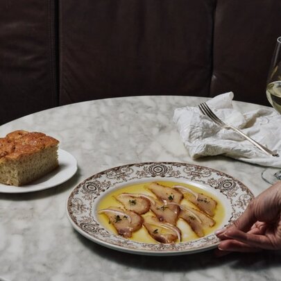 Waiter's hand placing a plate of cod on a marble table with a slice of cake and glass of white wine.