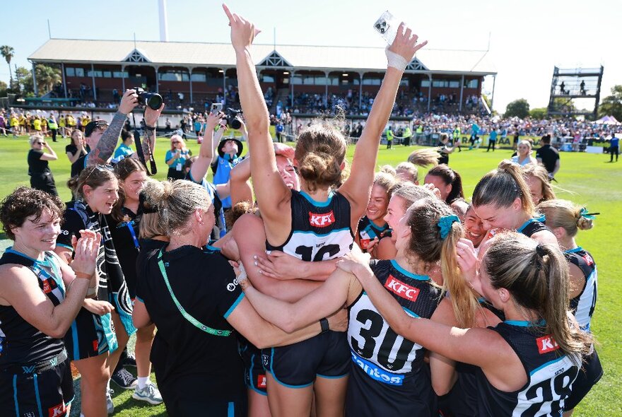 Football team celebrating on the ground with members in a huddle with arms raised in the air.