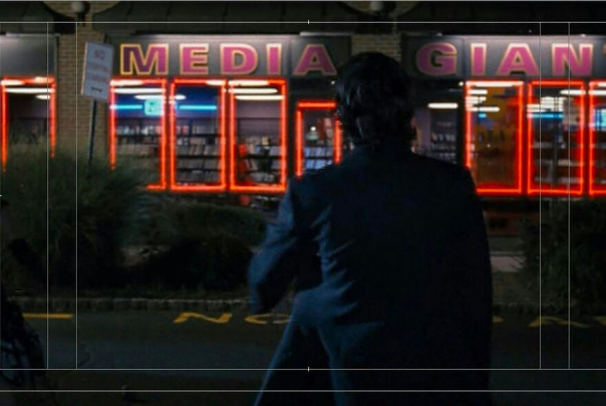 A still from the film Videoheaven, of a person standing outside a video hire store at night.