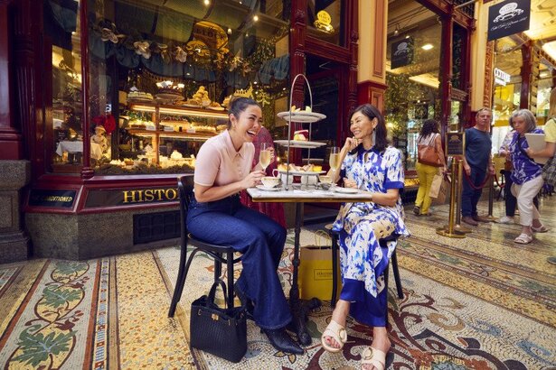 Two women laughing while they sit inside an arcade having high tea.