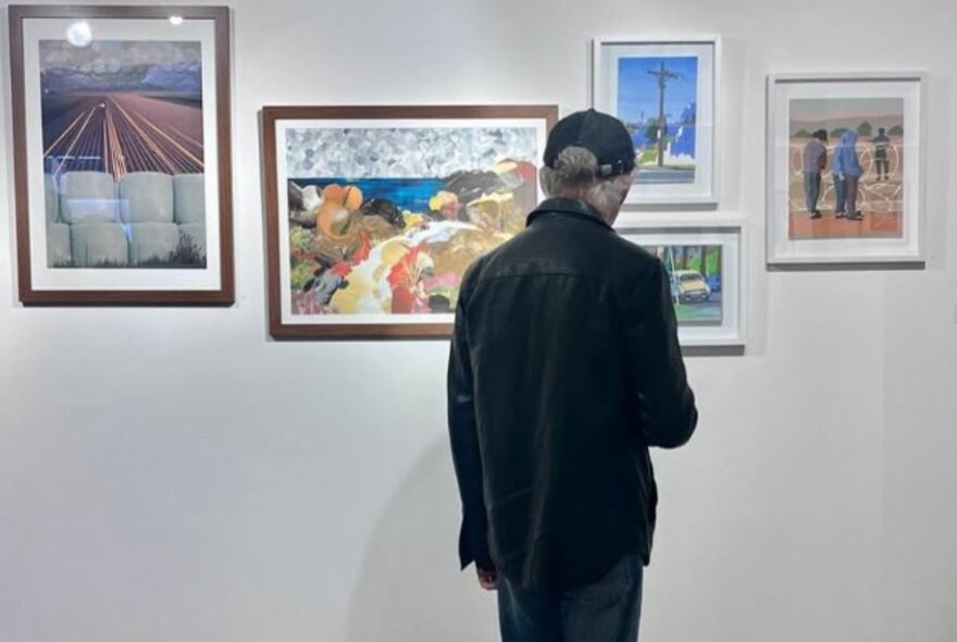 Person looking at framed artworks on a white gallery wall.
