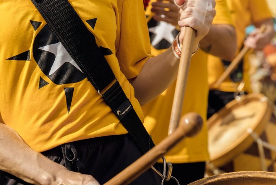 A close up of a person wearing a yellow t-shirt with a black star on it, and drumsticks in their hands.