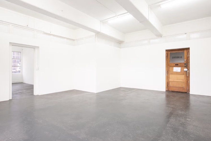 A stark, empty gallery space with a single wooden door-like structure. 