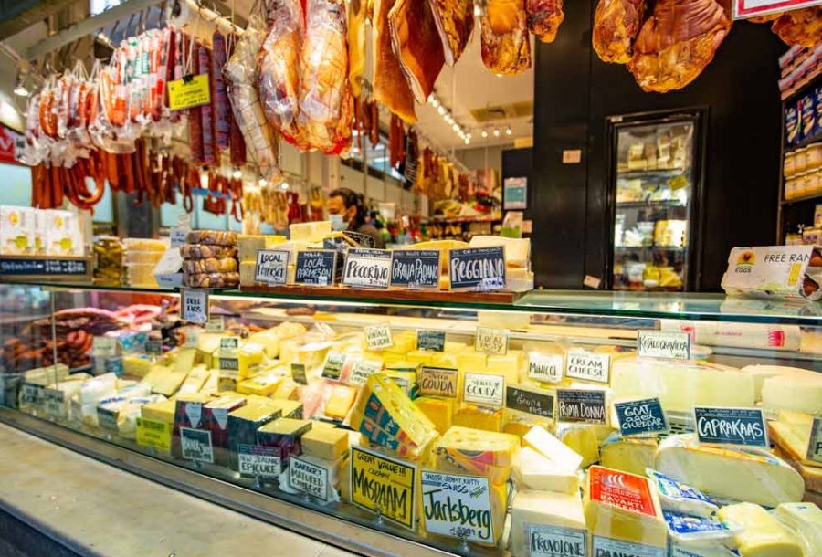 A selection of cheeses in a cabinet and meat hanging in a market stall.
